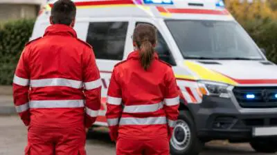 KI-Symbolbild: Zwei Personen in roten Warnschutzuniformen stehen vor einem Rettungswagen.