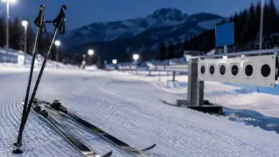 KI-generiertes Bild: Langlaufski und Stöcke auf einer beleuchteten Schneespur neben einer Biathlonzielanlage.