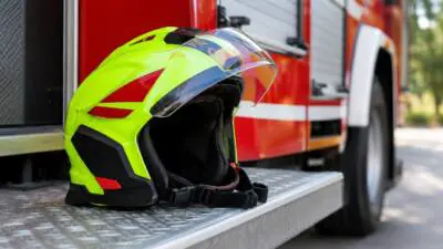 KI-generiertes Bild: Ein leuchtend gelbgrüner Schutzhelm liegt auf einer Metalltrittfläche vor einem roten Fahrzeug.