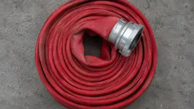 KI-Symbolbild: Aufgerollter roter Feuerwehrschlauch mit Metallkupplung auf grauem Boden.