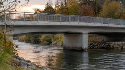 KI-generiertes Bild: Eine Betonbrücke mit Metallgeländer überspannt einen Fluss.