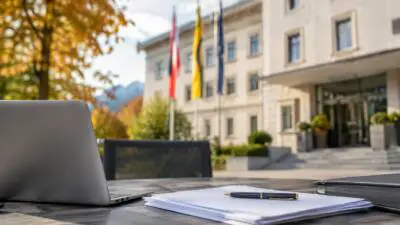 KI-Symbolbild: Ein Laptop und Unterlagen liegen auf einem Tisch vor einem hellen Gebäude mit Fahnen.