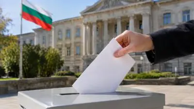 KI-Symbolbild: Eine Hand steckt einen weißen Stimmzettel in eine Wahlurne vor einem Säulengebäude.