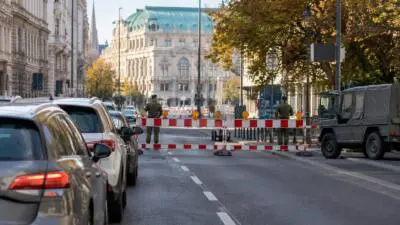 KI-Symbolbild: Absperrgitter sperren eine innerstädtische Straße; Autos und ein Geländewagen stehen davor.