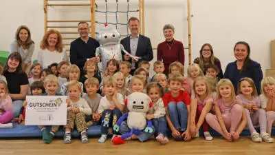 Kinder und Erwachsene posieren in einem Innenraum mit einem Roboter und einem großen Gutschein.