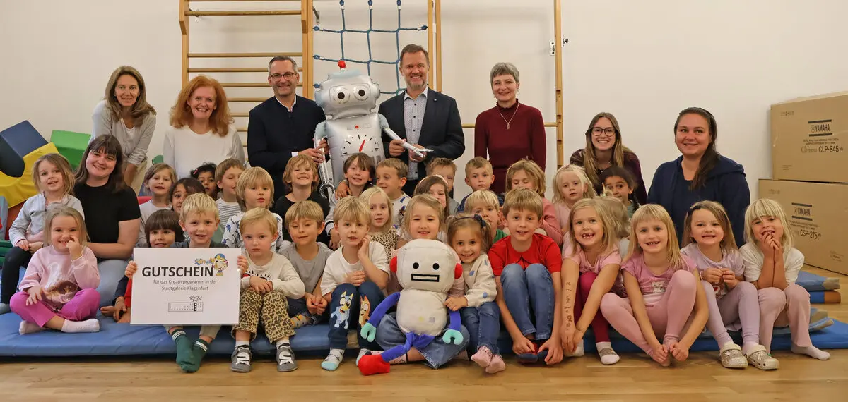 Kinder und Erwachsene posieren in einem Innenraum mit einem Roboter und einem großen Gutschein.