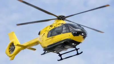 KI-Symbolbild: Ein gelber Hubschrauber fliegt vor blauem Himmel.
