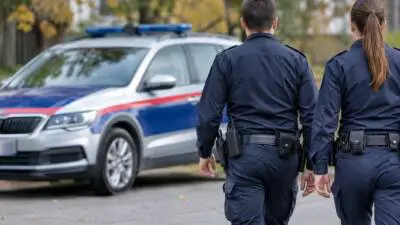 KI-Symbolbild: Uniformierte Personen stehen neben einem blau-weißen Fahrzeug mit blauem Leuchtbalken.