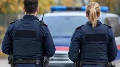 KI-generiertes Bild: Zwei uniformierte Personen stehen vor einem weißen Fahrzeug mit blauem Leuchtbalken.