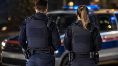 KI-Symbolbild: Zwei Personen in dunkler Uniform vor einem blau-weißen Fahrzeug mit Blaulicht.