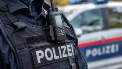 KI-generiertes Bild: Eine Polizeiweste mit Funkgerät vor einem unscharfen Polizeiauto.