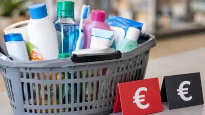 KI-generiertes Bild: Ein Einkaufskorb voller Drogerieartikel steht neben Preisschildern mit Eurozeichen.