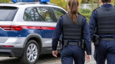 KI-Symbolbild: Uniformierte Personen stehen neben einem silbernen Wagen mit Blaulichtbalken.