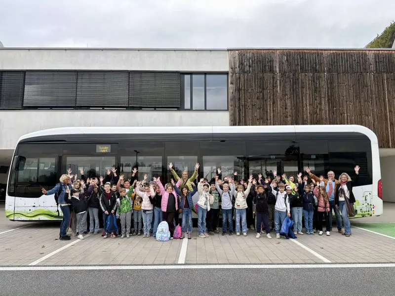 Eine Schülergruppe winkt vor einem Bus; die KMG erprobt in Klagenfurt einen Elektrobus im Alltag.