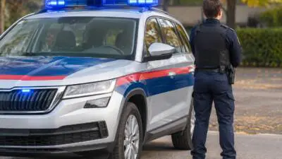 KI-Symbolbild: Ein weißes Fahrzeug mit blauem Leuchtbalken steht neben einer uniformierten Person.