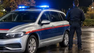 KI-Symbolbild: Eine uniformierte Person steht neben einem silbernen Auto mit blauem Lichtbalken.