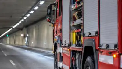 KI-Symbolbild: Ein rotes Einsatzfahrzeug mit geöffneten Geräteräumen in einem beleuchteten Straßentunnel.