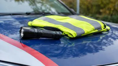 KI-generiertes Bild: Eine Warnweste und eine Taschenlampe liegen auf der Motorhaube eines blau-weißen Autos.
