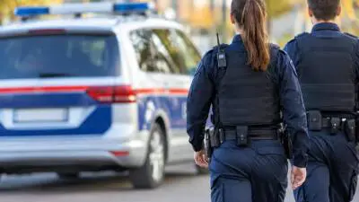 KI-Symbolbild: Uniformierte gehen neben einem blau-weißen Fahrzeug mit Blaulichtbalken.