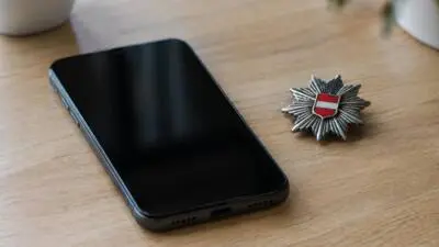 KI-Symbolbild: Ein schwarzes Smartphone liegt neben einem sternförmigen Abzeichen auf einem Holztisch.