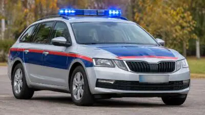 KI-generiertes Bild: Ein silberner Kombi mit blau-roter Markierung und blauem Blaulicht steht auf einer Straße.