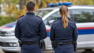 KI-Symbolbild: Uniformierte Personen vor einem Fahrzeug mit blauem Lichtbalken.