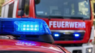 KI-Symbolbild: Blaues Blaulicht auf einem roten Fahrzeug vor einem Feuerwehrfahrzeug.