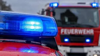 KI-generiertes Bild: Blaues Blaulicht auf einem roten Fahrzeug vor einem Feuerwehrfahrzeug.