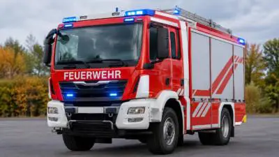KI-generiertes Bild: Ein rotes Feuerwehrfahrzeug mit blauem Blinklicht auf befestigter Fläche.