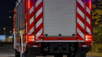 KI-generiertes Bild: Rückansicht eines rot-weißen Einsatzfahrzeugs mit leuchtenden Warnlichtern bei Nacht.