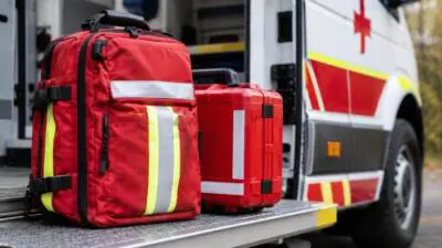 KI-Symbolbild: Rote Notfalltasche und roter Koffer auf der Trittstufe eines weiß-roten Rettungswagens.