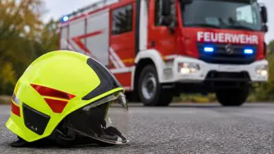 KI-Symbolbild: Ein gelber Feuerwehrhelm liegt vor einem roten Feuerwehrfahrzeug.