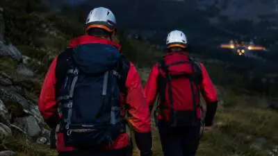 KI-generiertes Bild: Personen in roten Jacken mit Rucksäcken auf einem Bergpfad.