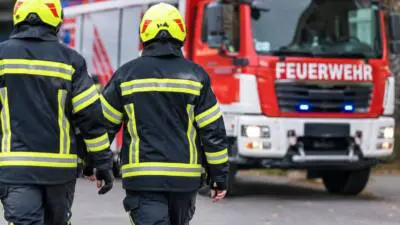 KI-Symbolbild: Feuerwehrleute in Schutzkleidung vor einem roten Feuerwehrfahrzeug.