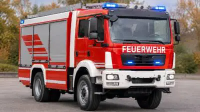 KI-Symbolbild: Rotes Feuerwehrfahrzeug mit leuchtendem Blaulicht auf einem gepflasterten Platz.