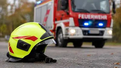 KI-generiertes Bild: Ein gelber Feuerwehrhelm liegt vor einem roten Feuerwehrfahrzeug.