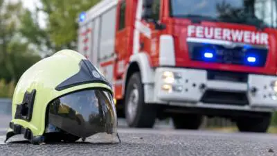 Ein gelber Feuerwehrhelm liegt vor einem roten Feuerwehrfahrzeug.