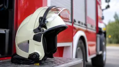 Ein heller Schutzhelm liegt auf einer Trittstufe vor einem roten Einsatzfahrzeug.