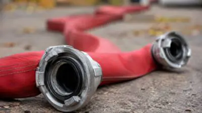 KI-Symbolbild: Ein roter Schlauch mit silbernen Metallkupplungen liegt auf rauem Boden.