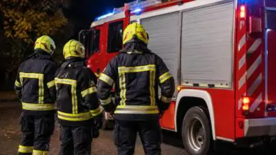 KI-Symbolbild: Personen in Schutzkleidung stehen neben einem roten Einsatzfahrzeug mit Blaulicht.