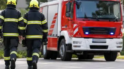 Einsatzkräfte in dunkler Schutzkleidung gehen auf ein rot-weißes Einsatzfahrzeug zu.