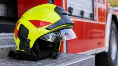 KI-generiertes Bild: Ein neongelber Helm liegt auf einer Metallstufe vor einem roten Einsatzfahrzeug.