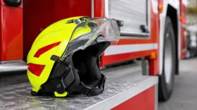 KI-Symbolbild: Neongelber Schutzhelm mit Visier liegt auf Metalltritt neben rotem Fahrzeug
