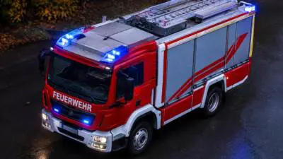 KI-generiertes Bild: Ein rotes Feuerwehrfahrzeug mit eingeschalteten Blaulichtern auf einer dunklen, nassen Straße.