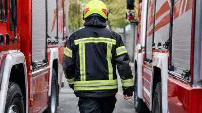 KI-generiertes Bild: Eine Einsatzkraft in dunkler Schutzkleidung steht zwischen roten Einsatzfahrzeugen.