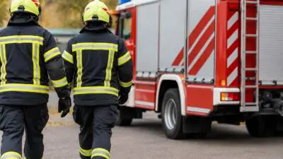 KI-Symbolbild: Feuerwehrleute in dunkler Schutzkleidung neben einem roten Feuerwehrfahrzeug.