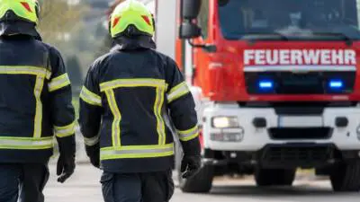 KI-Symbolbild: Feuerwehrleute in Schutzkleidung vor einem roten Feuerwehrfahrzeug.