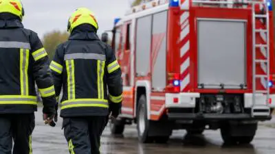 KI-Symbolbild: Feuerwehrleute in Schutzkleidung neben einem roten Einsatzfahrzeug.