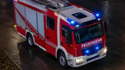 KI-Symbolbild: Ein rotes Feuerwehrfahrzeug mit eingeschaltetem Blaulicht auf nasser Straße.