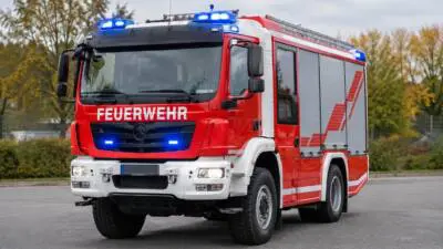 KI-Symbolbild: Ein rot-weißes Feuerwehrfahrzeug mit Blaulicht auf einer Straße.